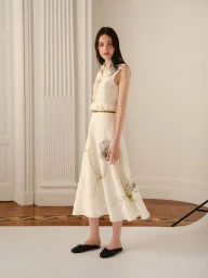 Model standing on white seamless floor wearing a sleeveless cream midi dress with floral illustrations
