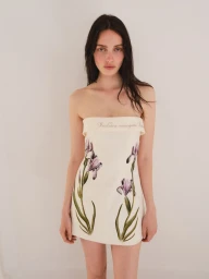 Model Clara Denison poses in a strapless off-white mini dress with botanical iris embroidery against a studio backdrop.