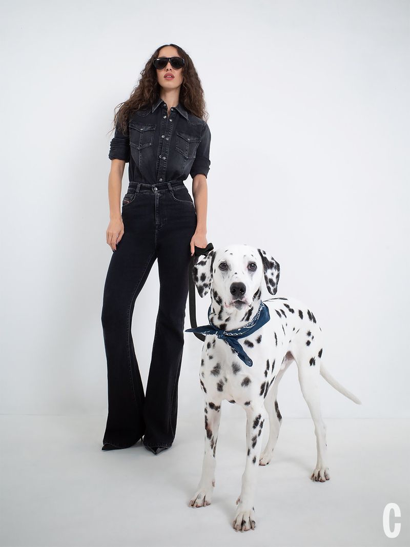 Model Alici Sol posing in double black denim with dark sunglasses next to a Dalmatian dog against a white background.
