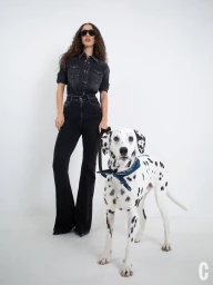 Model Alici Sol posing in double black denim with dark sunglasses next to a Dalmatian dog against a white background.