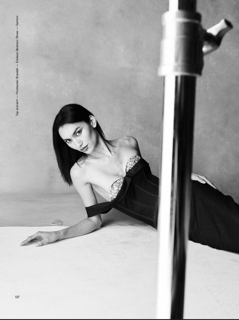 Model Jules Santiago reclining in a black strapless corset dress in a monochrome studio setting framed by a light stand.