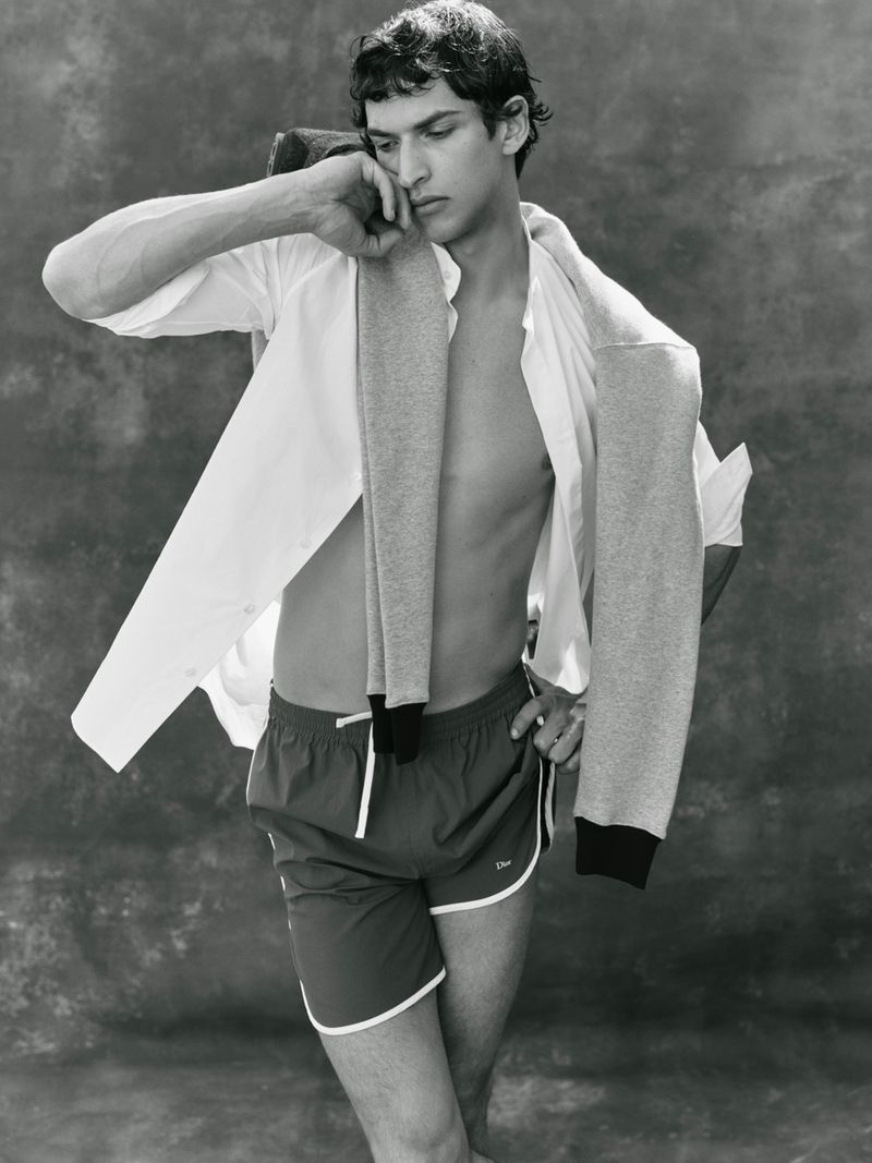 Black and white portrait of Habib Masovic posing in athletic shorts with an open white shirt and sweater draped over his shoulders.