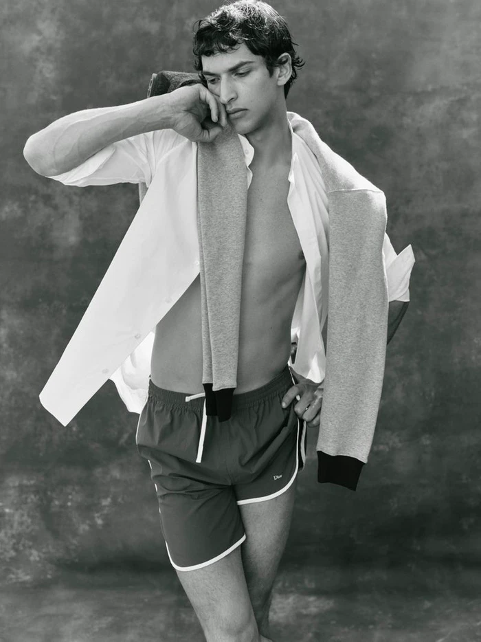 Black and white portrait of Habib Masovic posing in athletic shorts with an open white shirt and sweater draped over his shoulders.