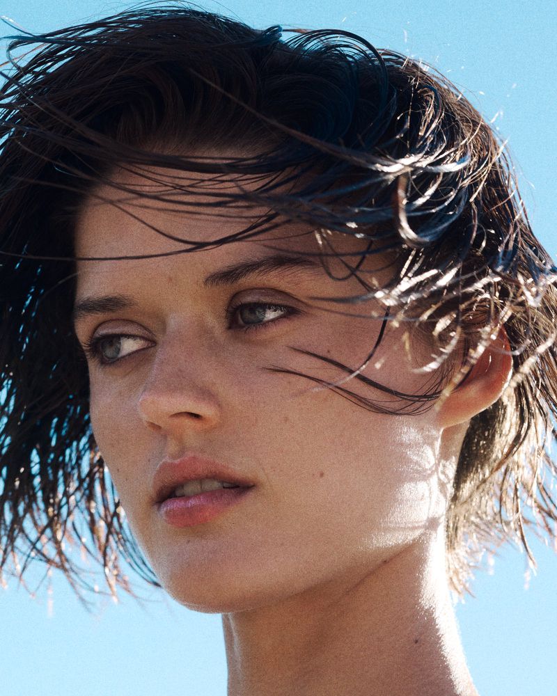 Close-up portrait of a woman with wet dark hair blowing in the wind against a clear blue sky