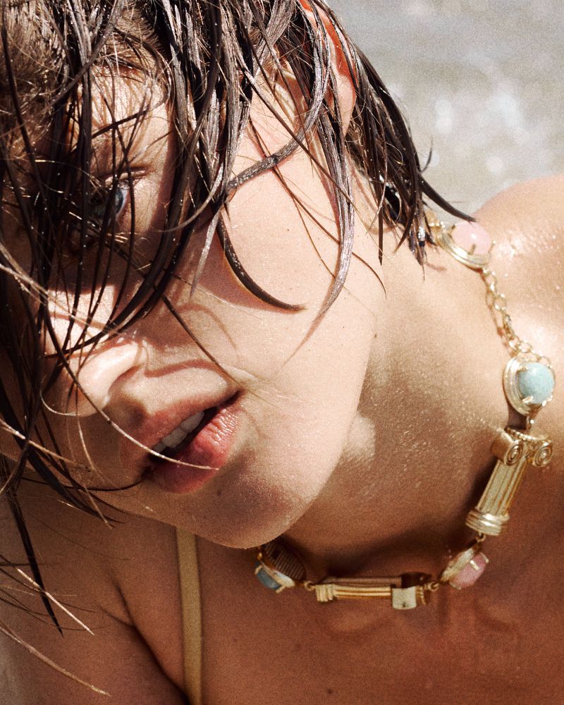 Close-up of model Bonnie Panasenko with wet hair wearing an architectural gold statement necklace with pastel stones.