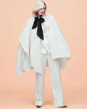 Raquel Zimmermann wearing an oversized white cape suit with a black bow tie against a solid peach background for W Magazine.