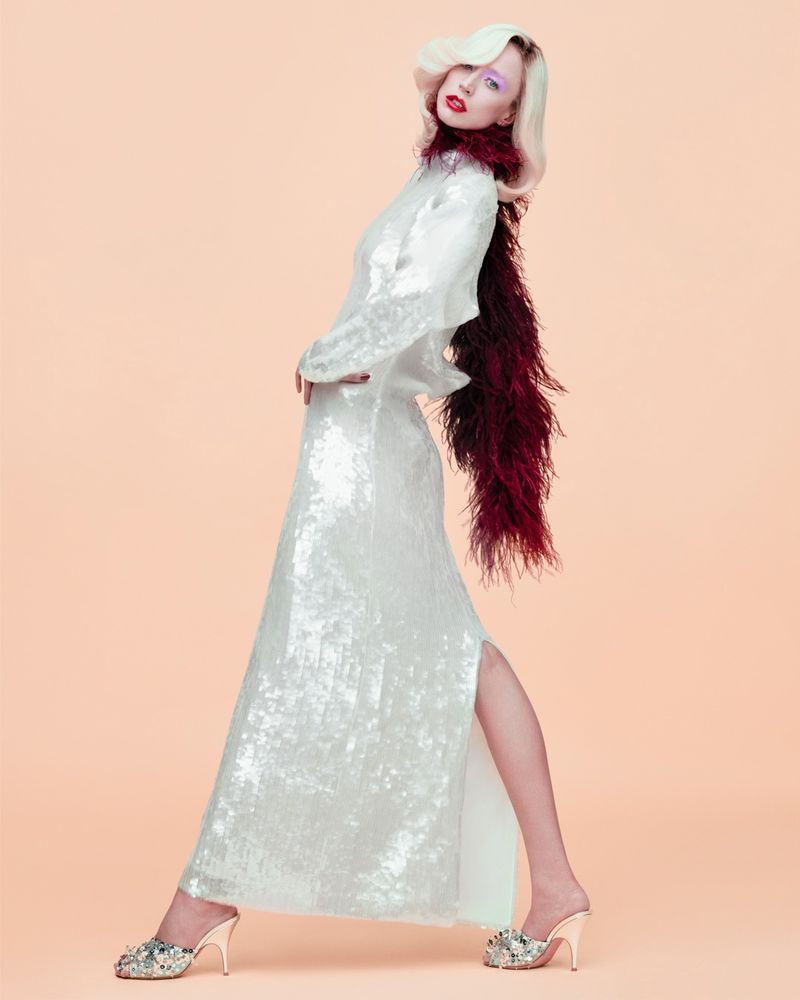 Model Raquel Zimmermann wearing a white sequin gown and burgundy feather boa against a peach background for W Magazine.