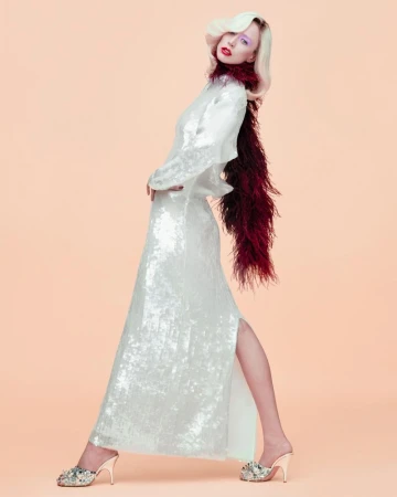 Model Raquel Zimmermann wearing a white sequin gown and burgundy feather boa against a peach background for W Magazine.