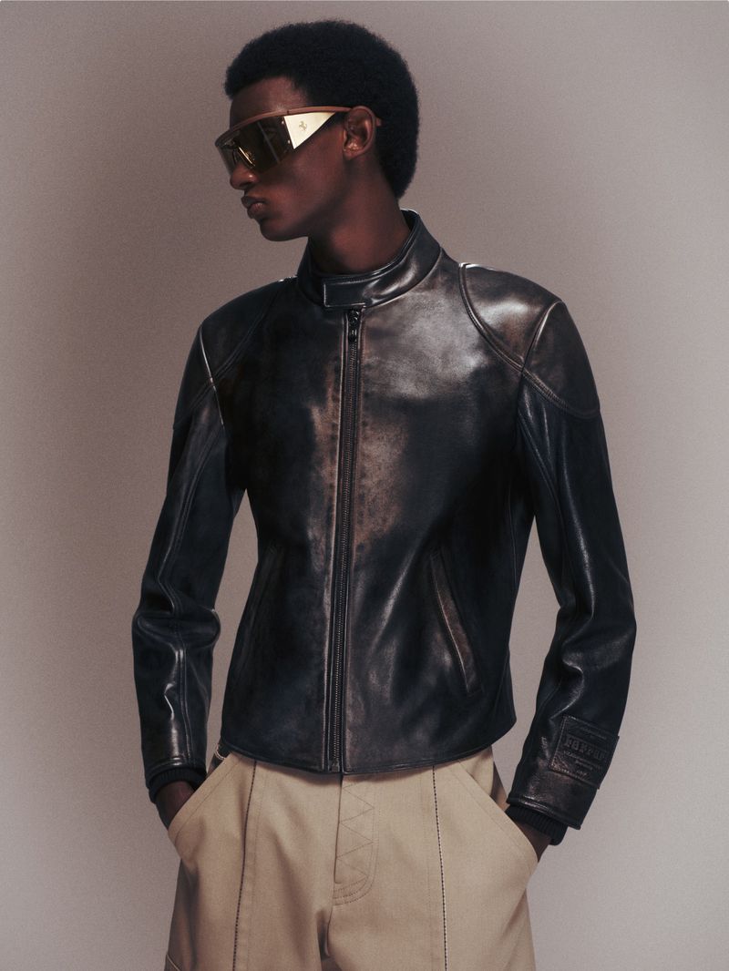 Model Yahne Ba wearing a black leather moto jacket and metallic visor sunglasses in a studio shoot for Ferrari.