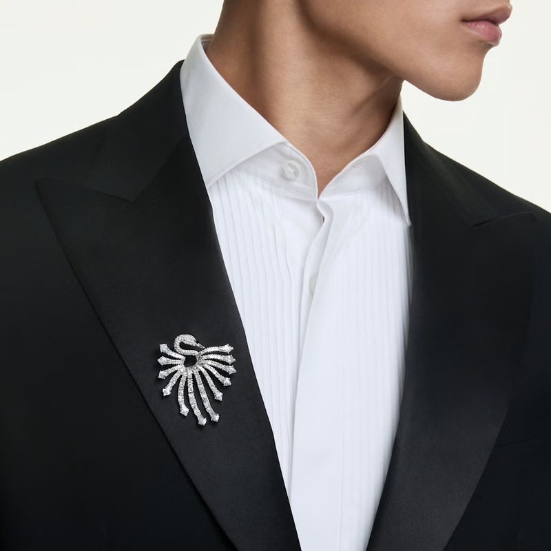 Close-up of a model in a black tuxedo jacket and white pleated shirt wearing a sparkling crystal swan brooch on the lapel.