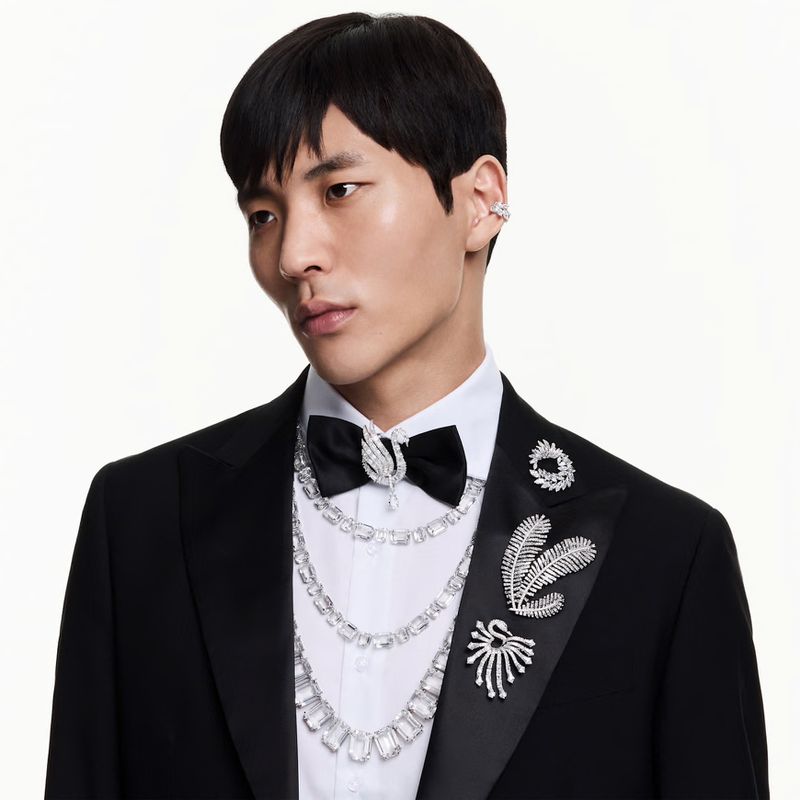 Model Horim Song in a black tuxedo with layered crystal necklaces and brooches against a white background