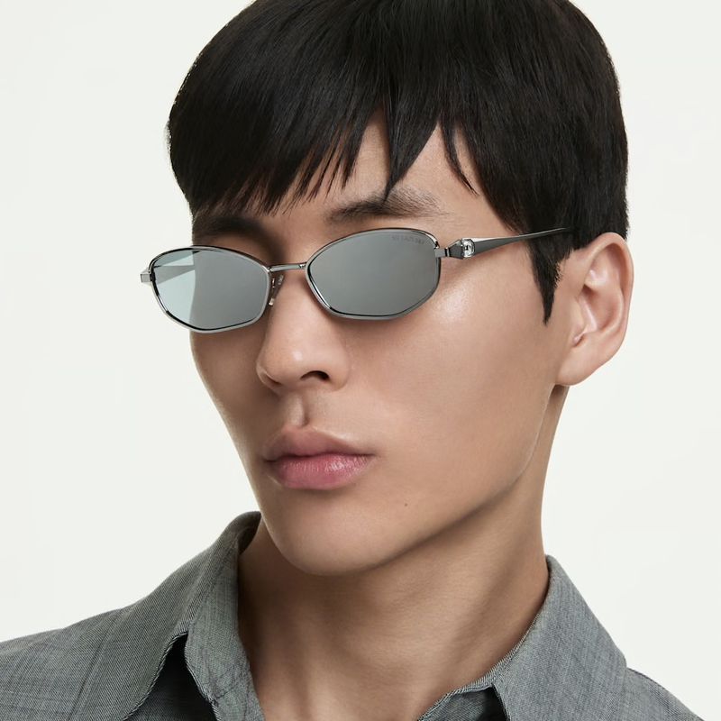 Close-up portrait of an Asian male model wearing silver geometric sunglasses and a grey collared shirt against a white backdrop.