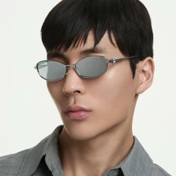 Close-up portrait of an Asian male model wearing silver geometric sunglasses and a grey collared shirt against a white backdrop.