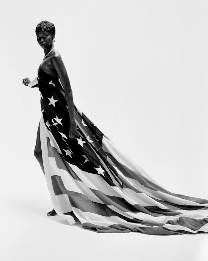 Anok Yai in a flowing American flag gown with a long train in black and white against a white studio background.