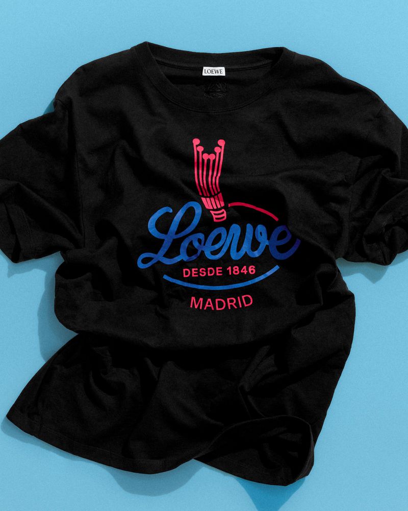 Black Loewe graphic t-shirt featuring blue script and red logo details laid flat against a vibrant light blue background.