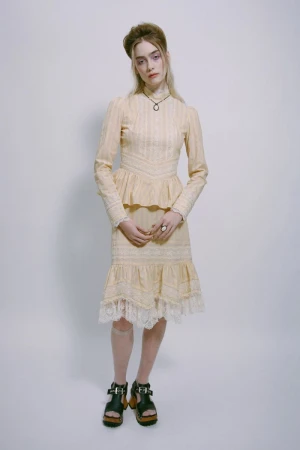 Model wearing a cream lace-trimmed dress with black platform sandals against a plain neutral background
