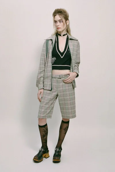 Model Ryleabeth wearing a plaid jacket and matching shorts with a black vest against a seamless white studio background
