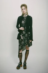 Model in black cardigan and patterned dress wearing knee-high socks against a white backdrop