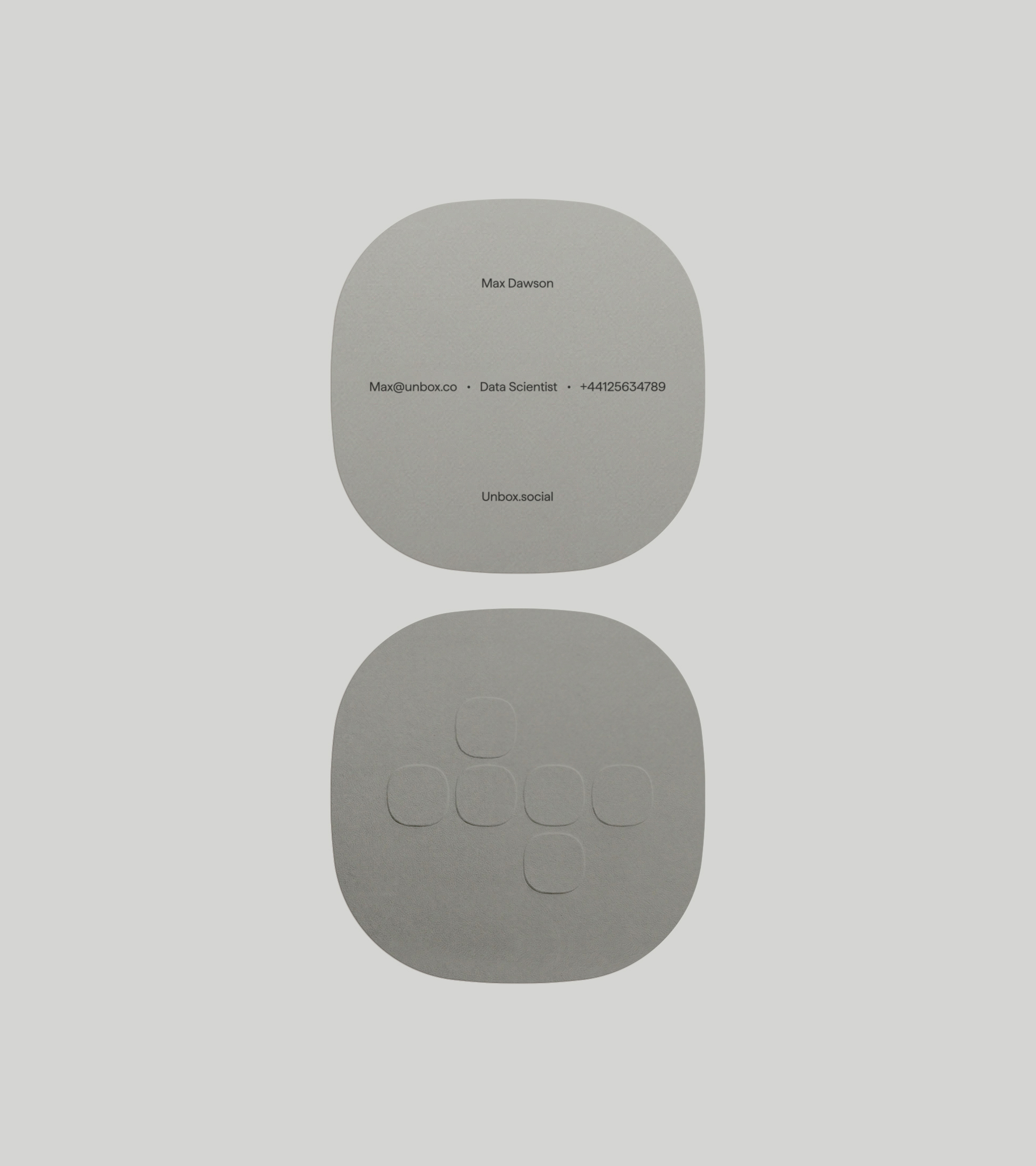 Rounded square grey business cards displaying typography and an embossed geometric logo for Unbox on a light grey background.
