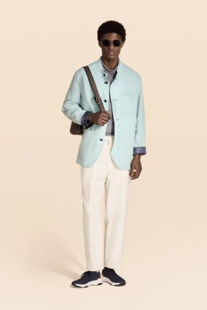 Model Aboubakar Konte in a light green jacket, white trousers, and sunglasses against a cream studio backdrop for Berluti.