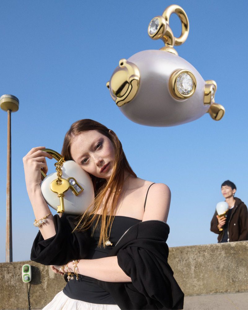 Model holding a heart-shaped padlock bag with a floating submarine charm against a clear blue sky