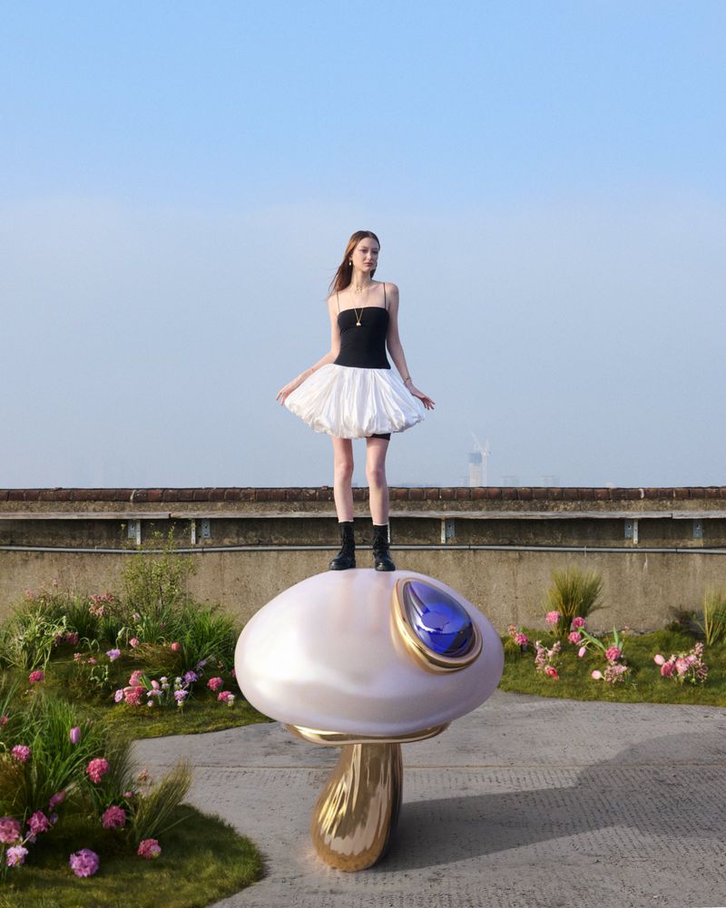 Model Bai standing atop an oversized sculptural mushroom with a jewel detail on a rooftop for Pandora.