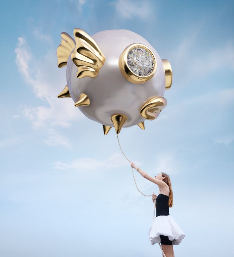 Model holding a string attached to a giant floating pearl and gold pufferfish balloon against a soft blue sky.