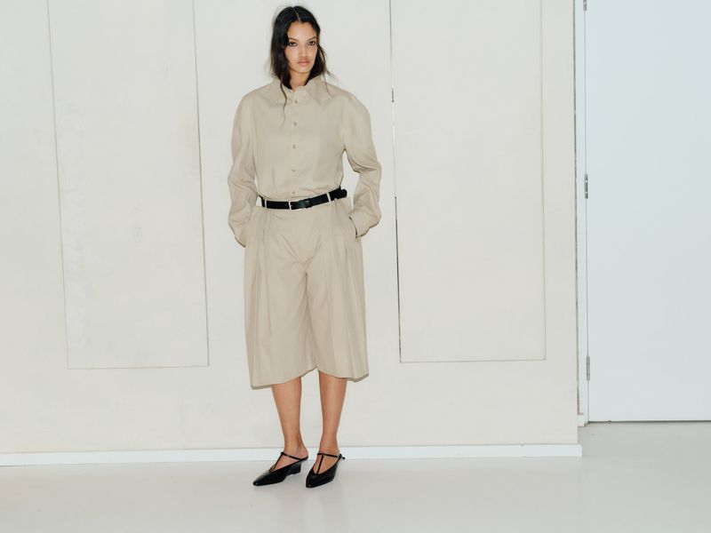 Model Corinne Murray wearing beige button-down shirt and matching trousers against plain white studio wall