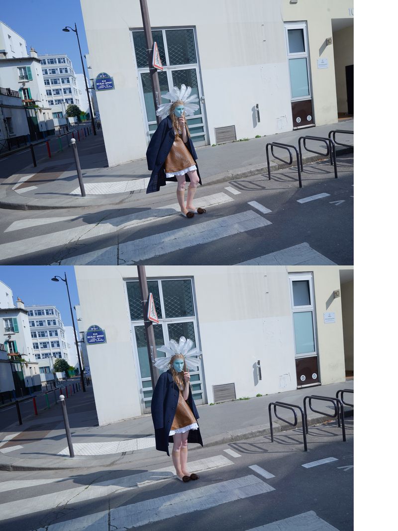 Model wearing a brown ruffled dress, navy coat, and white feather headpiece on a sunny Parisian street crosswalk.
