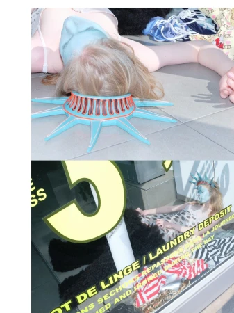 Model lying on the ground wearing a blue Statue of Liberty crown and face covering in a storefront window display.