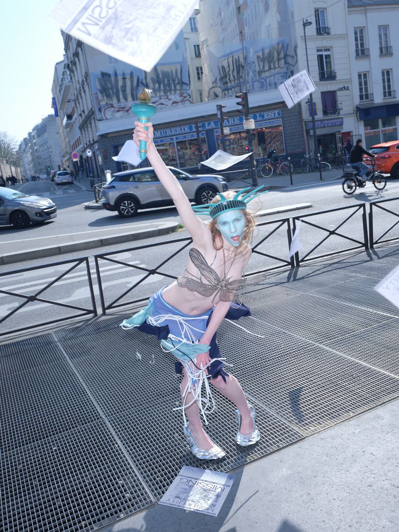 Model dressed as Statue of Liberty holding a torch on a city street with flying papers for Office Magazine editorial
