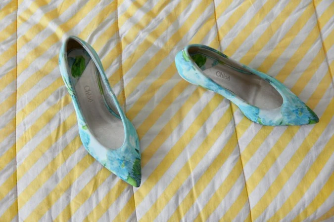 Pair of light blue floral pointed-toe Chloé flats resting on a yellow and white diagonal striped fabric background.