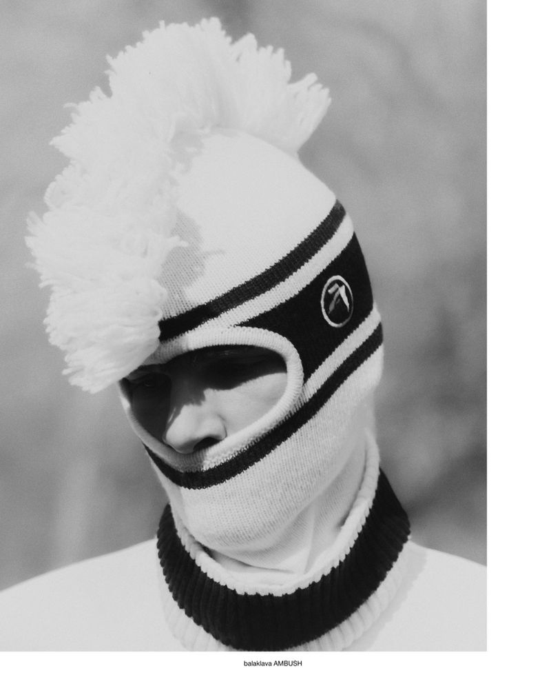 Model wearing a white knit balaclava with a large crest trim and black striped details in a black and white fashion portrait.