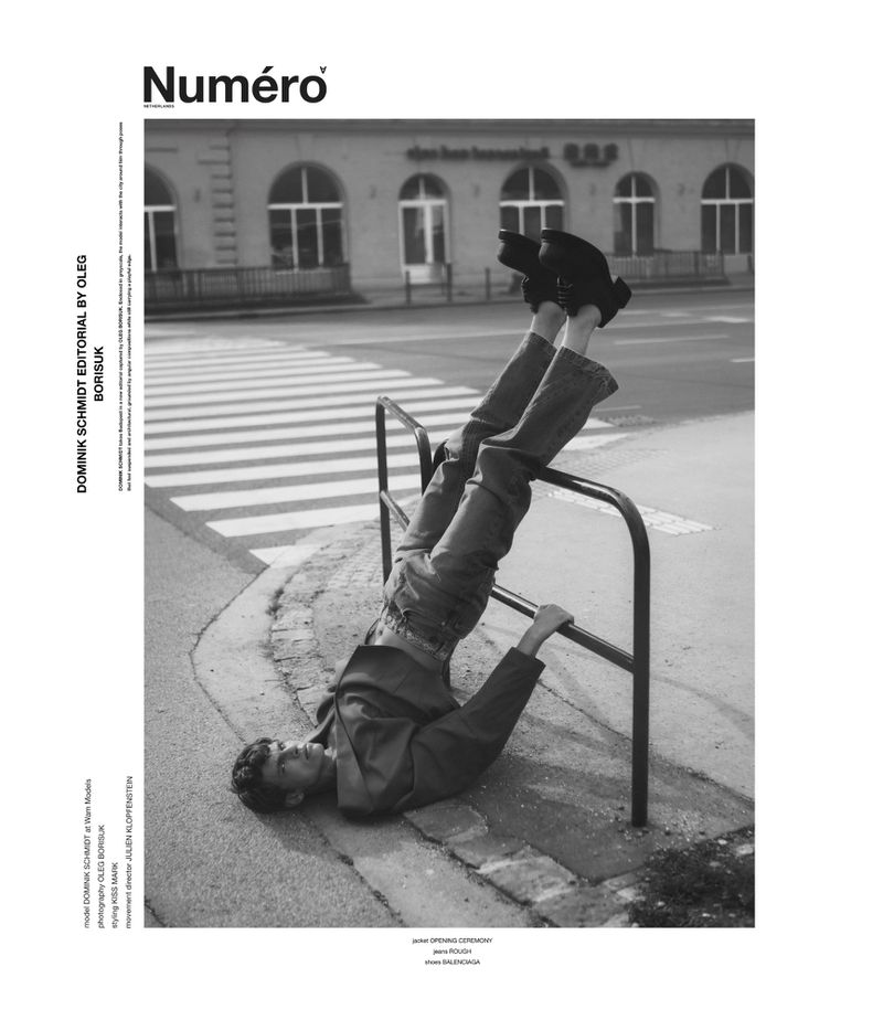 Model Dominik Schmidt lying upside down on the pavement resting his legs against a metal street railing in a black and white editorial.