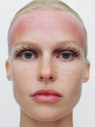 Close-up portrait of a woman with freckles, graphic drawn eyelashes, and a pink gradient across her forehead on a white background.