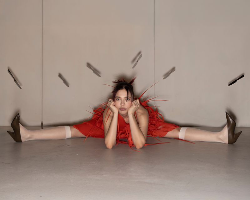Nina Kraviz performing a leg split in a red fringe dress with levitating knives in a studio shoot for King Kong Magazine.