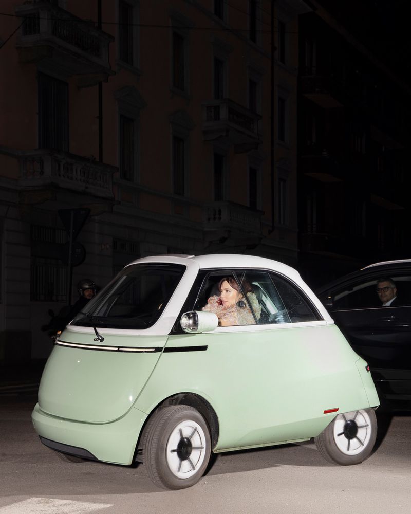 Nina Kraviz seated inside a pale mint green and white microcar on a city street at night.