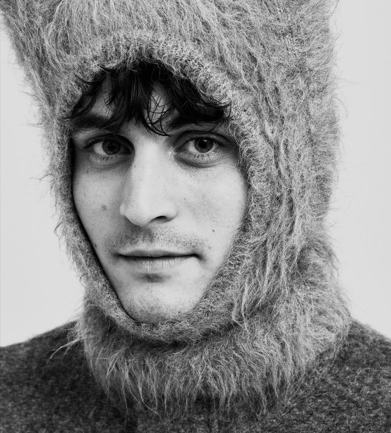 Black and white close-up portrait of Julien De Saint-Jean wearing a fuzzy textured knit balaclava hood and matching sweater.