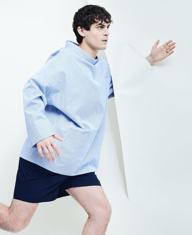 Julien De Saint-Jean wearing a light blue pinstripe shirt and navy shorts in a dynamic pose against a white backdrop.