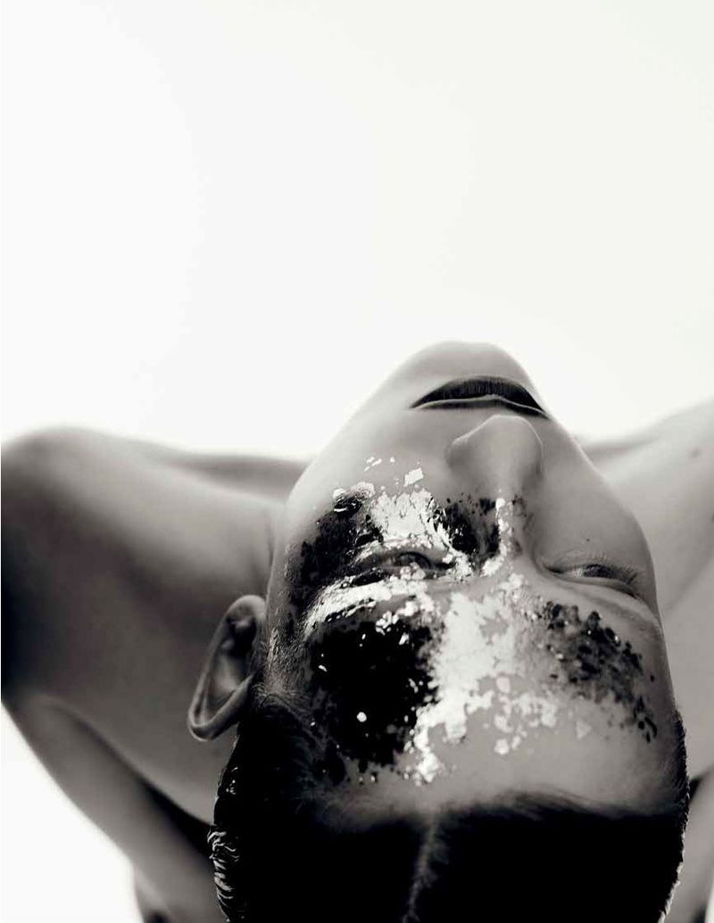 Black and white beauty portrait of Melinda Kiss with dark pigment and metallic flakes across her face against a white background.