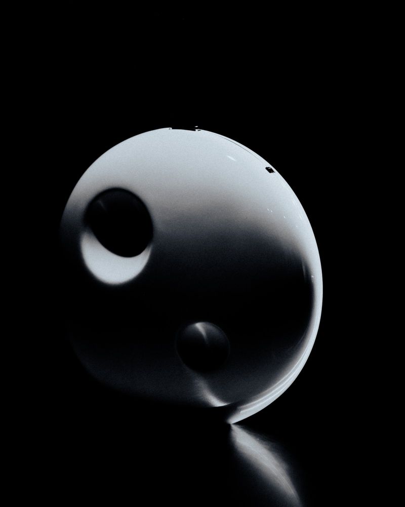 Sculptural white spherical headpiece with circular indentations lit against a solid black background.