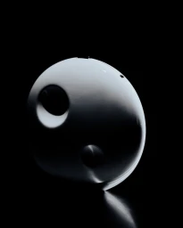 Sculptural white spherical headpiece with circular indentations lit against a solid black background.