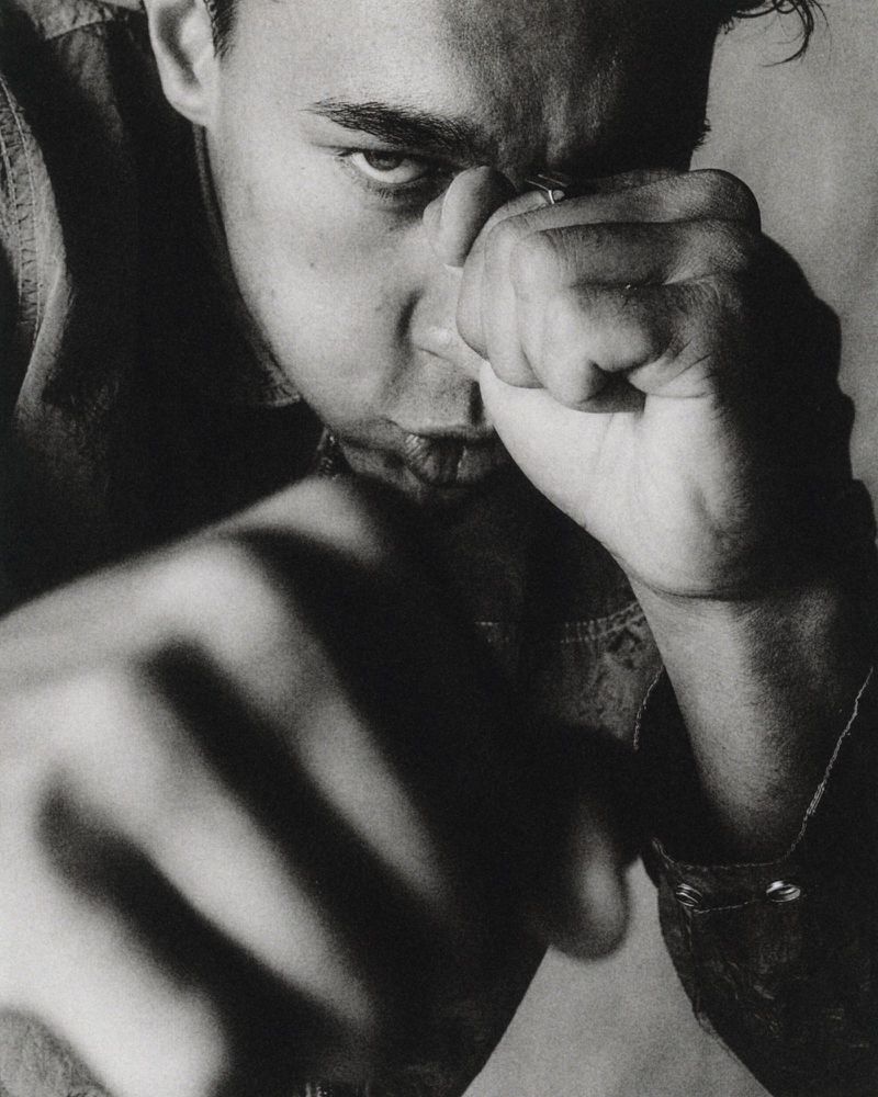 Black and white close-up portrait of a man raising his clenched fists in a combat stance toward the camera.