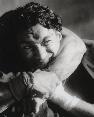 Black and white close-up portrait of a smiling man held in an arm lock with wrapped wrists.