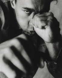 Black and white close-up portrait of a man raising his clenched fists in a combat stance toward the camera.