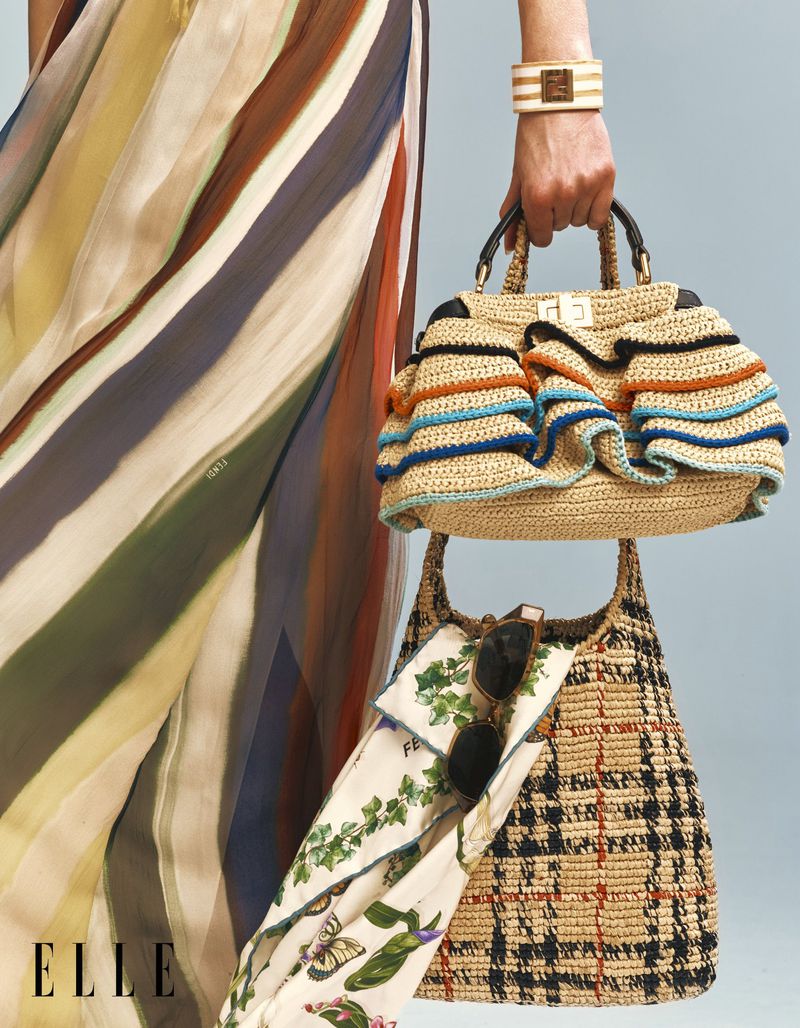 Close-up of a model holding a tiered ruffled raffia handbag alongside a woven check tote and multi-colored striped fabric.