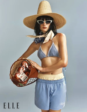 Model Hannah Vincent wearing a tall straw hat, white sunglasses, and a light blue crochet bikini holding a fruit basket.