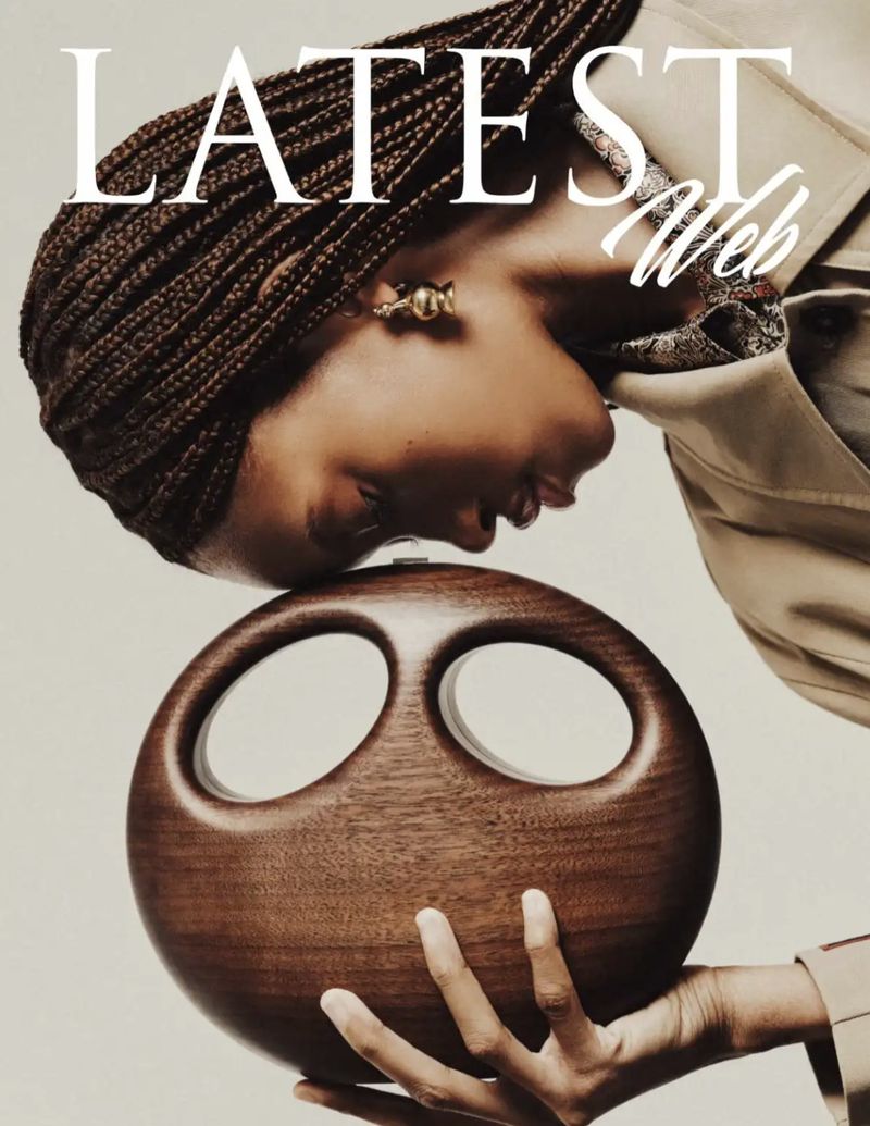 Model with braided hair holding a dark carved wooden round handbag against a plain background