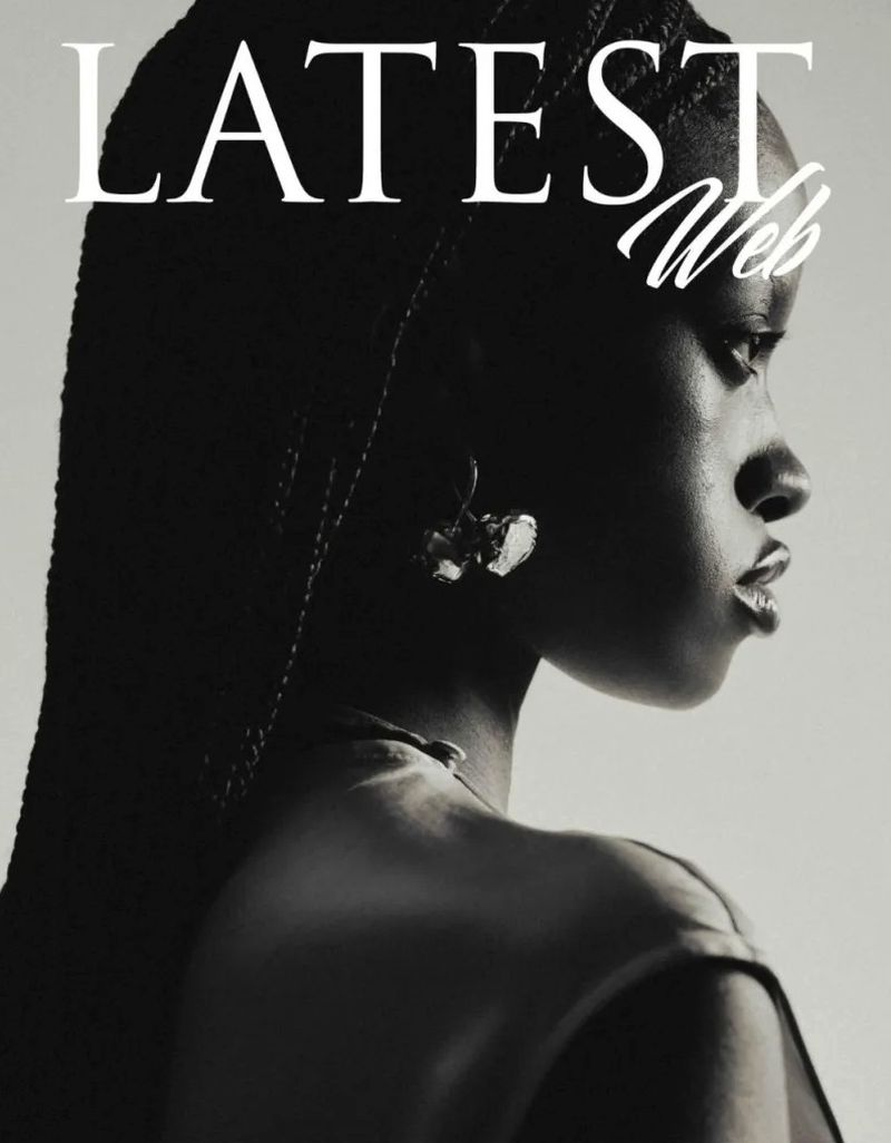 Black and white profile portrait of a Black woman with braided hair wearing a sculptural earring against a grey backdrop.