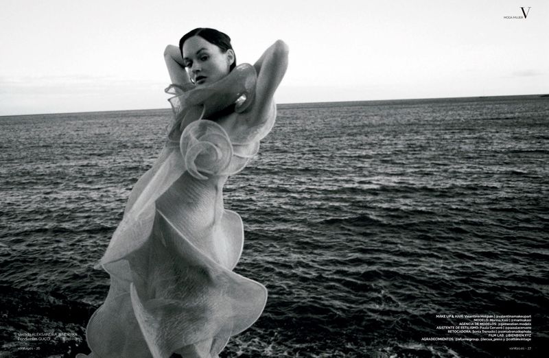 Woman in a sheer sculptural ruffled dress posing against the open sea in a black and white editorial shoot.